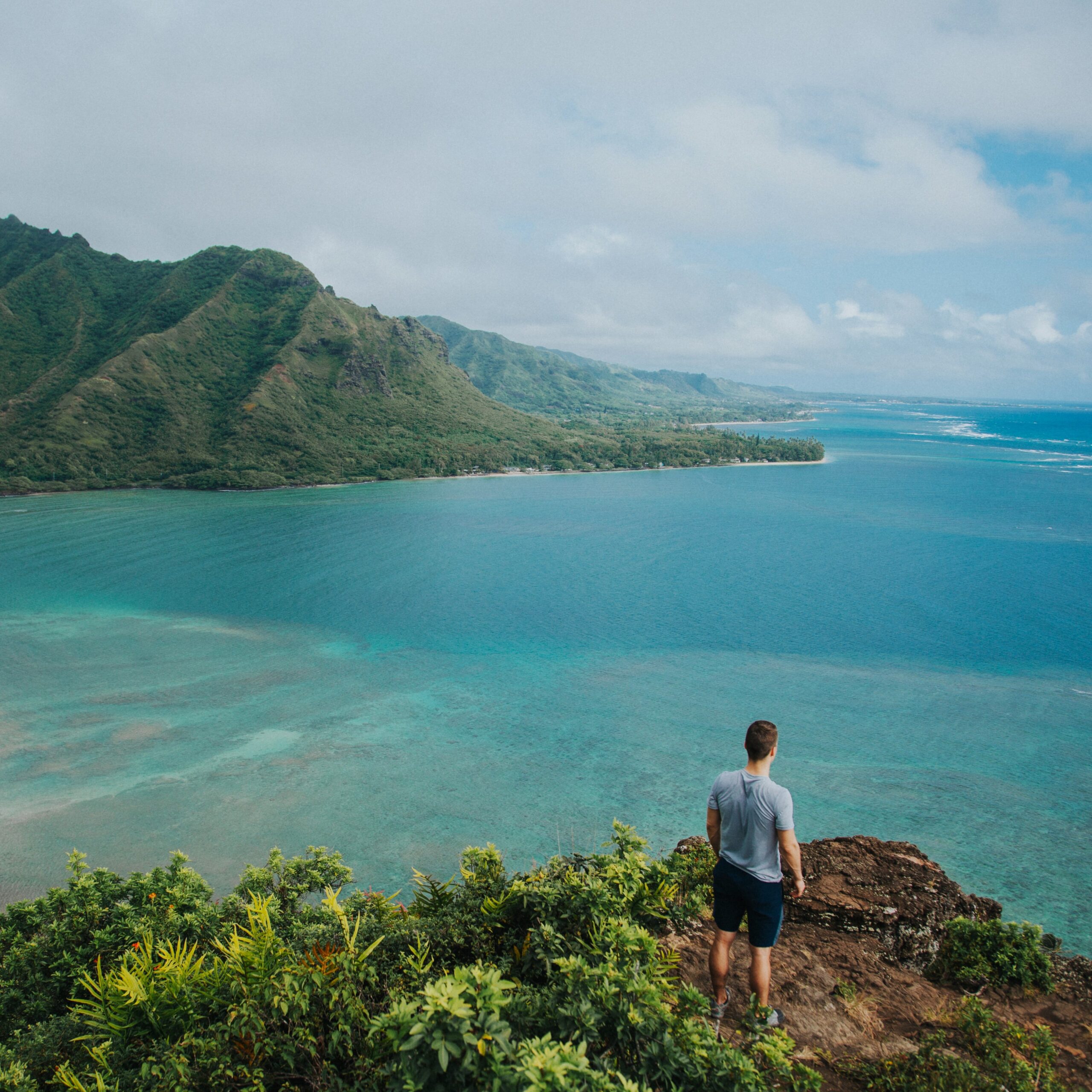 Person standing on a scenic mountain in Maui trail with sunshine and greenery.